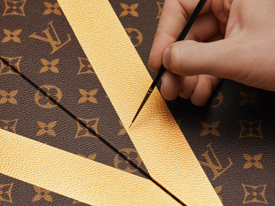 Louis Vuitton kézműves ecsettel festi az arany V betűt a monogramos vászonra