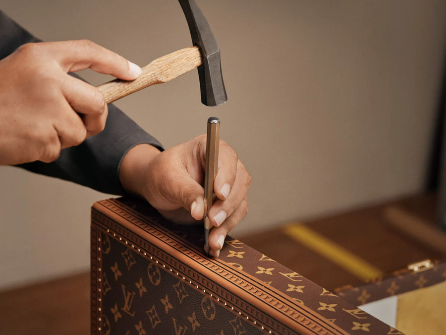 Louis Vuitton kézműves kalapáccsal rögzíti a sárgaréz szegecseket a láda bőrszegélyén