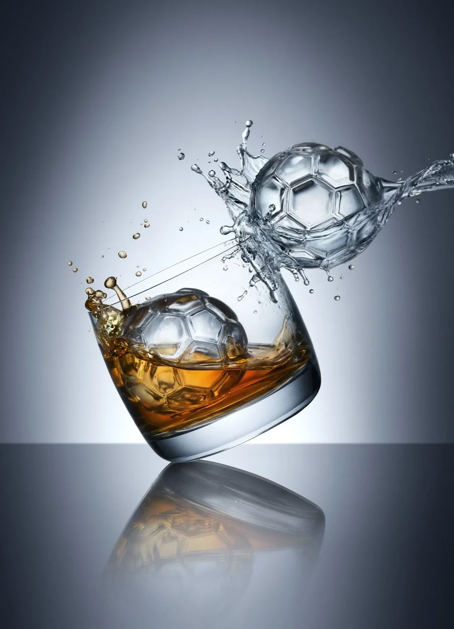 Focilabdát mintázó jéggömb whiskyspohárban, fröccsenő vízzel