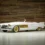 Fehér színű, nyitott Cadillac Elegante roadster aranyozott díszítőelemekkel fa háttér előtt