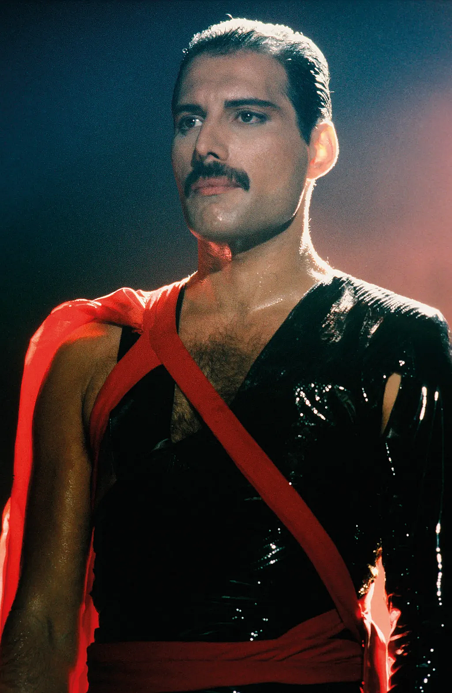 Freddie Mercury bajusszal, fényes fekete felsőben és vörös szalaggal átkötve