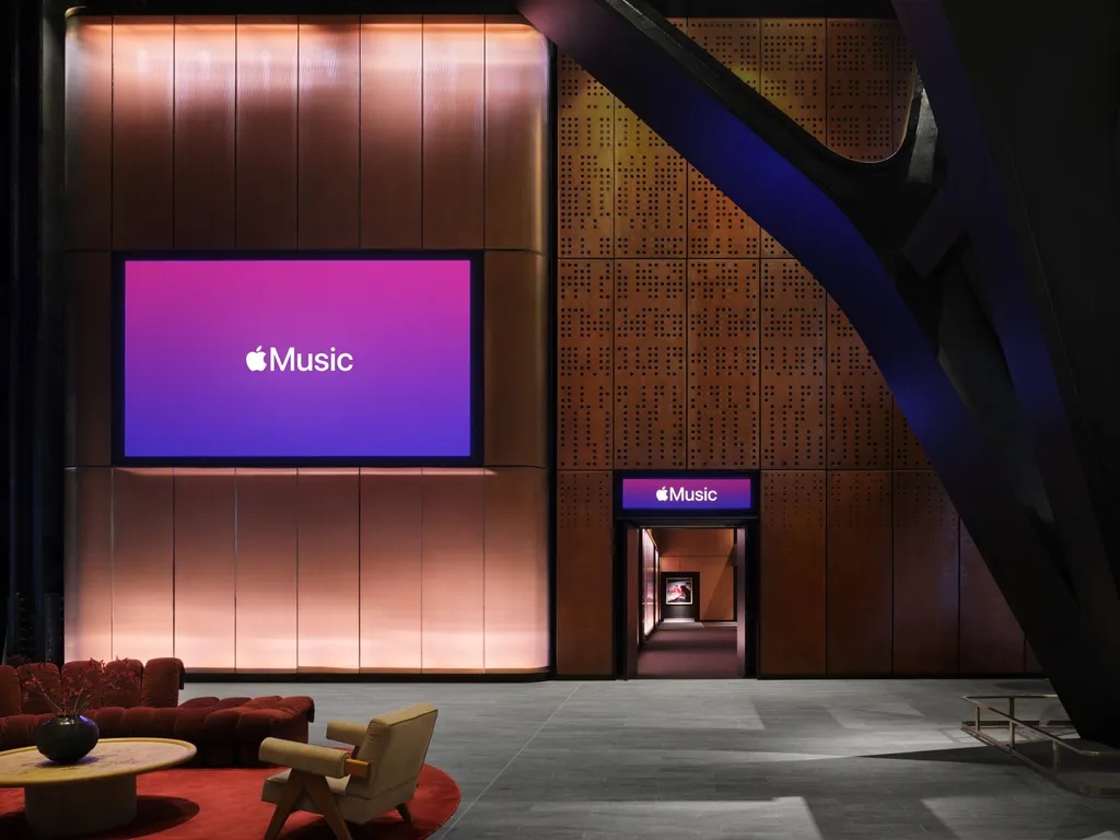 Nagy méretű Apple Music feliratú kijelző fémburkolatú falon kanapéval és fotellel